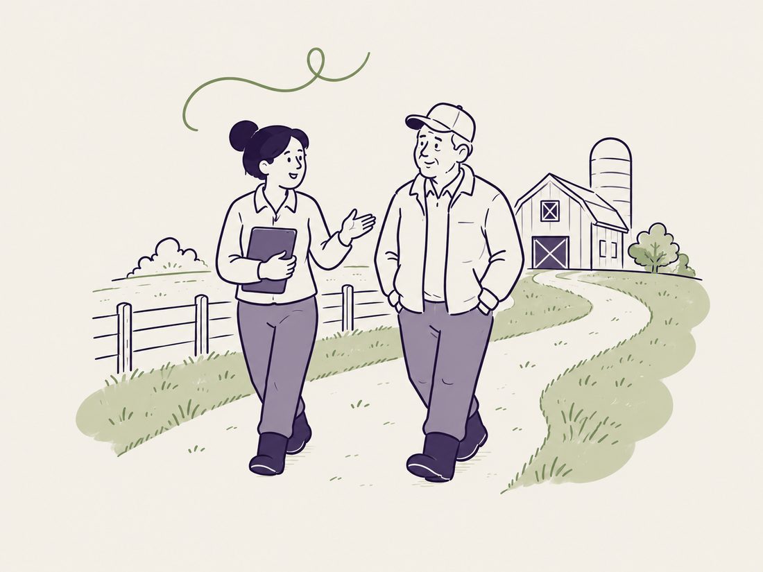 A farm professional and a farmer walking a path together, talking, with a barn in the distance.